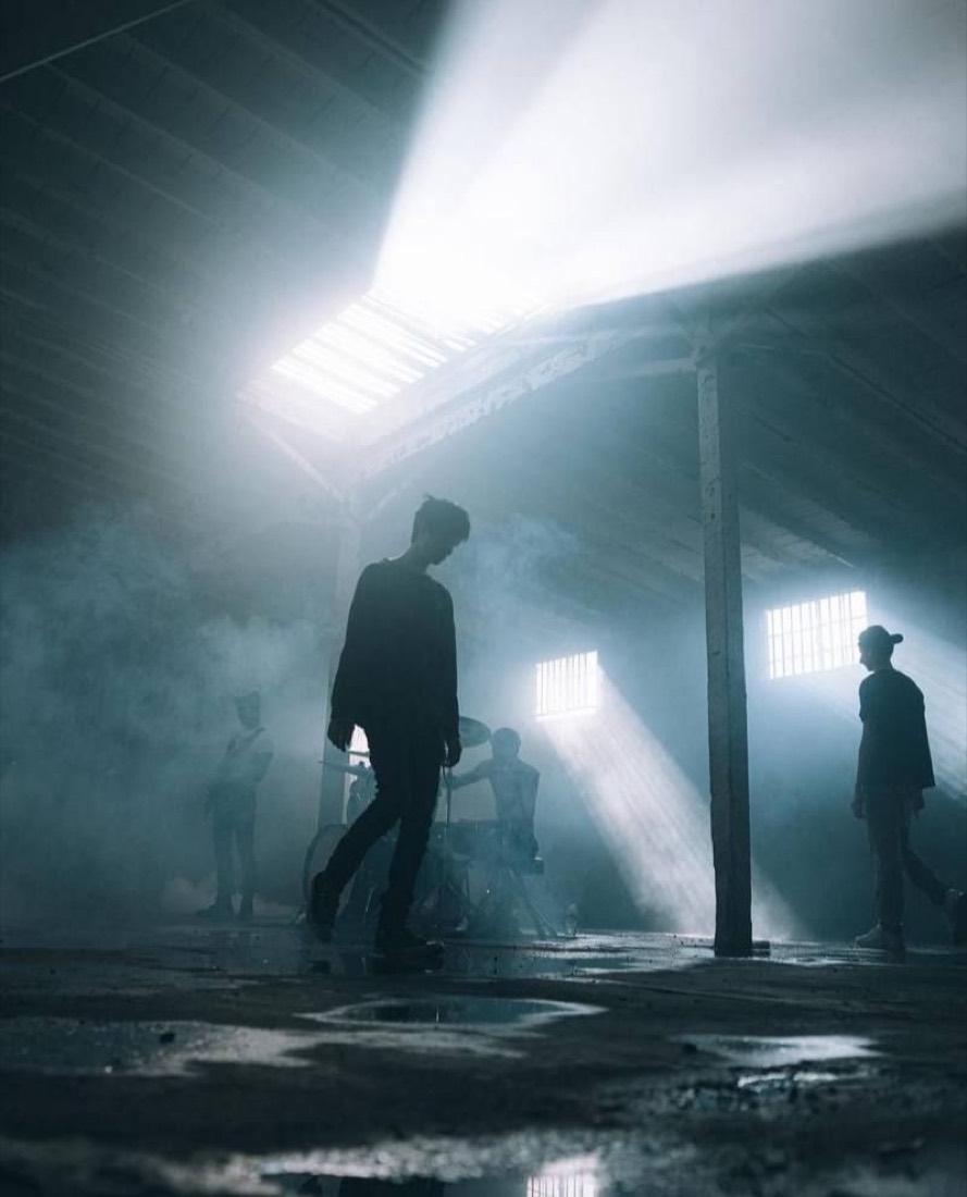 Artistas en una bodega industrial atravesada por rayos de luz.