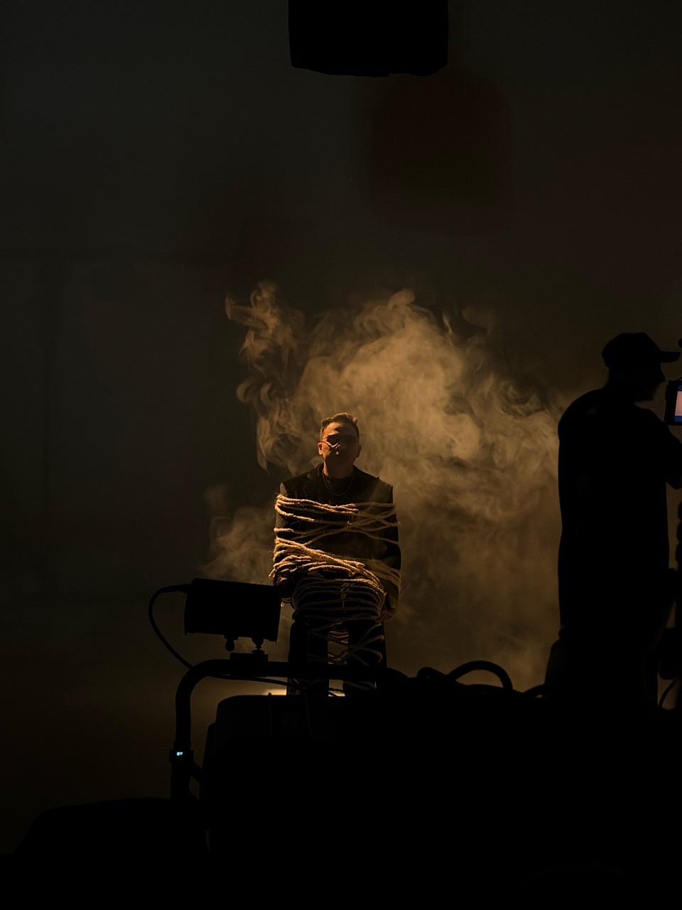 Artista iluminado entre humo y siluetas del equipo durante la grabación.